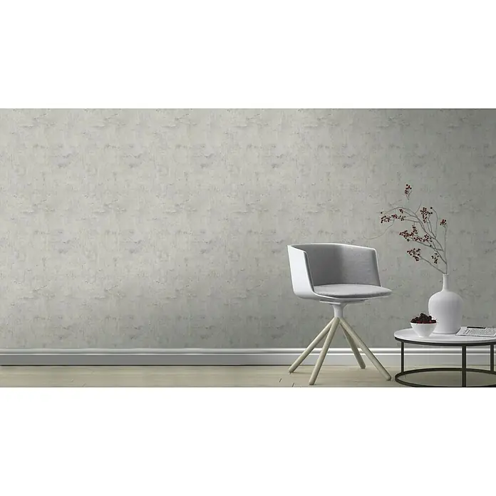 Rasch Tapetenwechsel Vliestapete - Grau, Betonoptik, 10,05 x 0,53 m - Ein stilvolles Interieur mit einem modernen Stuhl, einem kleinen Tisch und dekorativen Elementen vor einer strukturierten Wand.