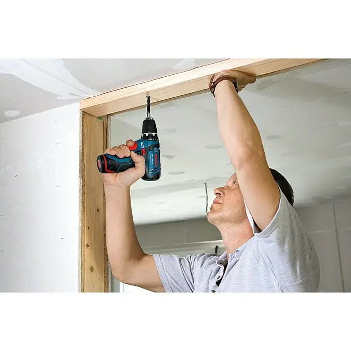 Bosch Professional Taladro atornillador percutor de batería GSB 12V-15 - 12 V, 2 baterías, 2 Ah, 30 Nm, 2 baterías y cargador - Un hombre trabaja en una estructura de madera con un taladro/atornillador inalámbrico Bosch. La herramienta es compacta y potente.