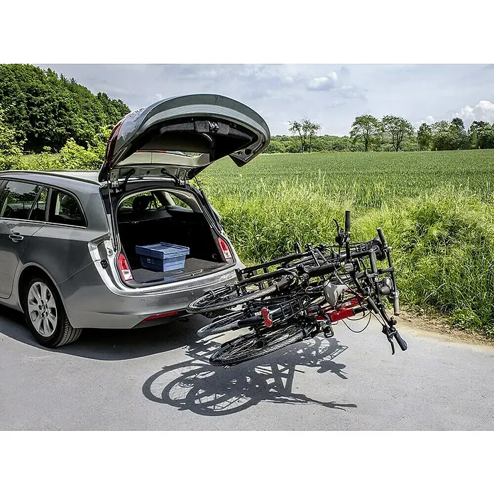 Eufab Fahrradträger Amber III - Geeignet für: 3 Fahrräder, Passend für: Fahrzeuge mit Anhängerkupplung - Silberner Kombi mit geöffneter Heckklappe und Fahrradträger mit Fahrrädern, steht auf einer Straße neben einem grünen Feld.