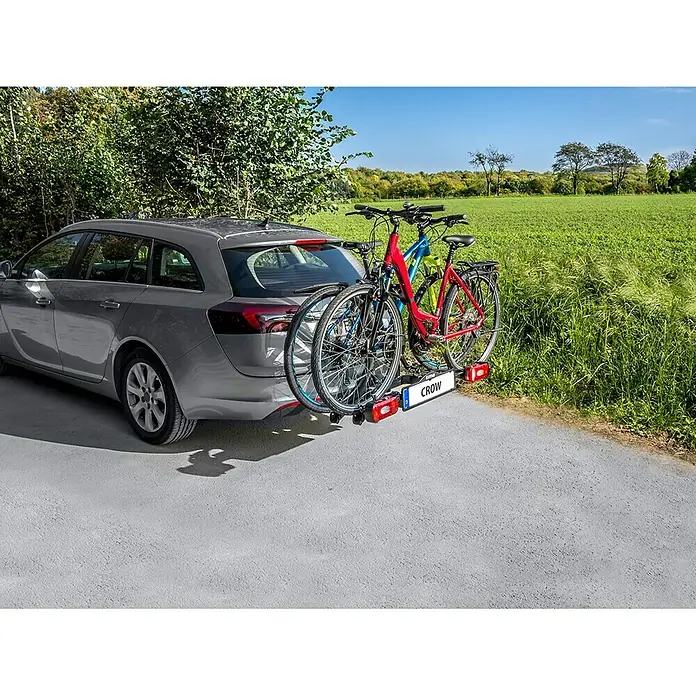 Eufab Fahrradträger Crow - Geeignet für: 2 Fahrräder, Max. Ladegewicht: 50 kg, Passend für: Fahrzeuge mit Anhängerkupplung - Ein graues Auto mit einem CROW Fahrradträger am Heck, auf dem zwei Fahrräder befestigt sind, vor einer grünen Landschaft.