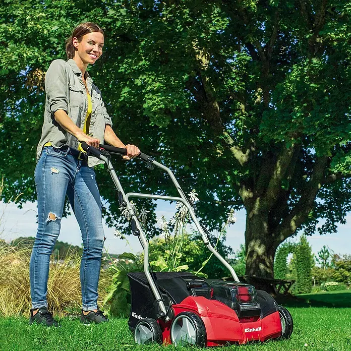 Einhell Power X-Change 18V Akku-Vertikutierer GE-SC 35/1 Li-Solo - Anzahl Akkus: Ohne Akku, 36 V, Arbeitsbreite: 35 cm - Eine Frau benutzt einen roten Einhell Rasenlüfter im Garten, um den Rasen zu pflegen.