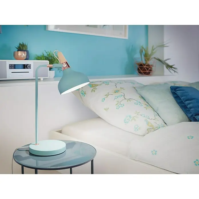 Paulmann Neordic Tischleuchte Juna - 20 W, Softgrün, E14 - Blaue Schreibtischlampe mit Holzdetails auf einem Nachttisch neben einem Bett, das eine gemütliche und stilvolle Schlafzimmeratmosphäre schafft.
