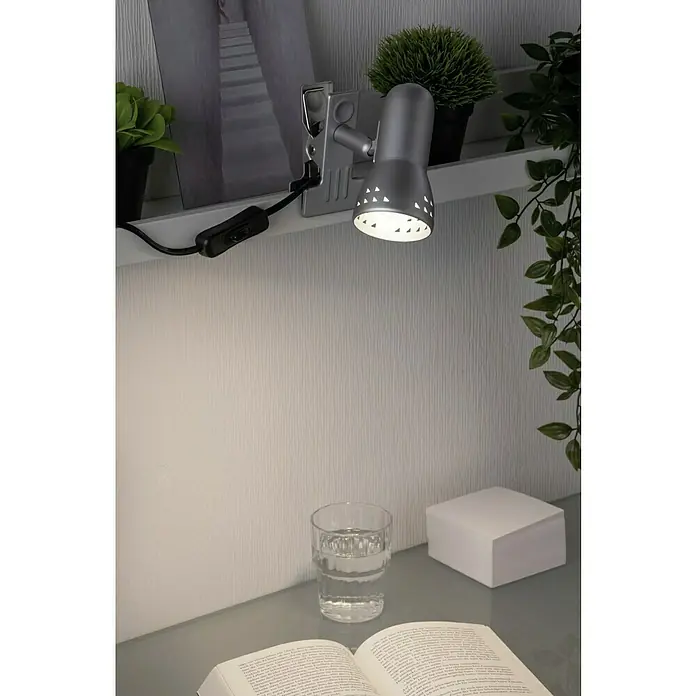 Paulmann Klemmspot Gryps - 40 W, Silber - Nahaufnahme einer silberfarbenen Klemmlampe, die Licht auf ein Buch, ein Glas Wasser und einen Notizblock auf einem Tisch wirft.