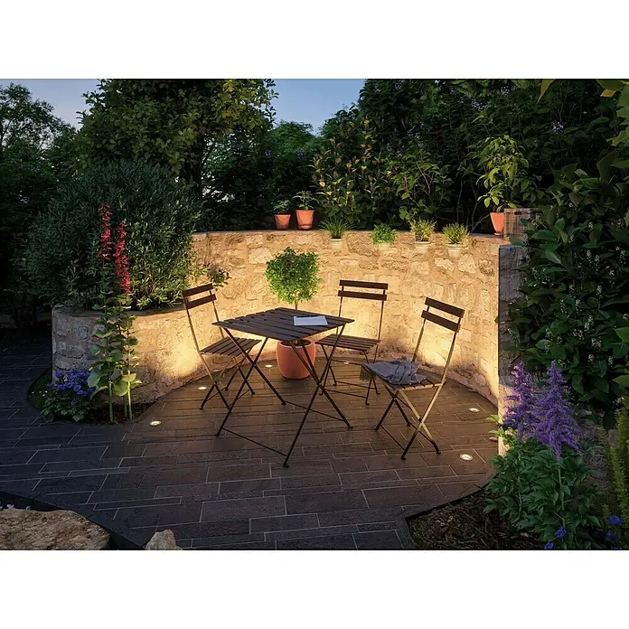 Paulmann Plug & Shine LED-Gartenspot-Set Floor Mini Ergänzung - 3 Stk., 24 V, 2,5 W, IP65 - Einladende Gartenszene mit einem stilvollen Gartentischset, umgeben von üppigem Grün und stimmungsvoller Beleuchtung für entspannte Stunden im Freien.