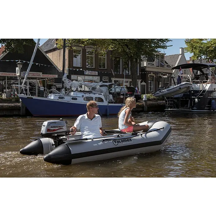 Talamex Schlauchboot Luftboden Aqualine QLA270 - L x B: 270 x 152 cm, Tragkraft: 410 kg, Geeignet für: 3 Personen - Ein Talamax Aqualine Schlauchboot wird auf einem Kanal von einem Mann und einem Mädchen gefahren, mit Häusern und Booten im Hintergrund.
