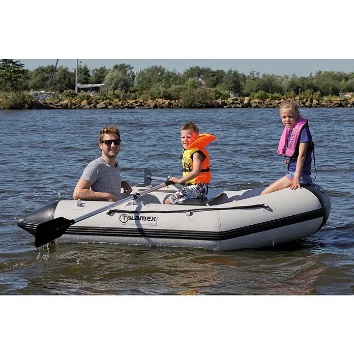 Talamex Schlauchboot Luftboden Aqualine QLA250 - L x B: 250 x 152 cm, Tragkraft: 400 kg, Geeignet für: 2+1 Personen - Ein graues Talamex-Schlauchboot gleitet auf dem Wasser, mit drei Personen an Bord, alle mit Schwimmwesten für die Sicherheit ausgestattet.