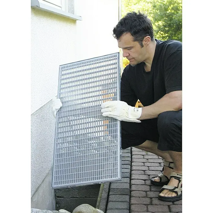 Schellenberg LichtschachtabdeckungStahl - Mann setzt einen Kellerfensterrost ein. Der robuste Gitterrost schützt den Keller vor Laub und Ungeziefer.