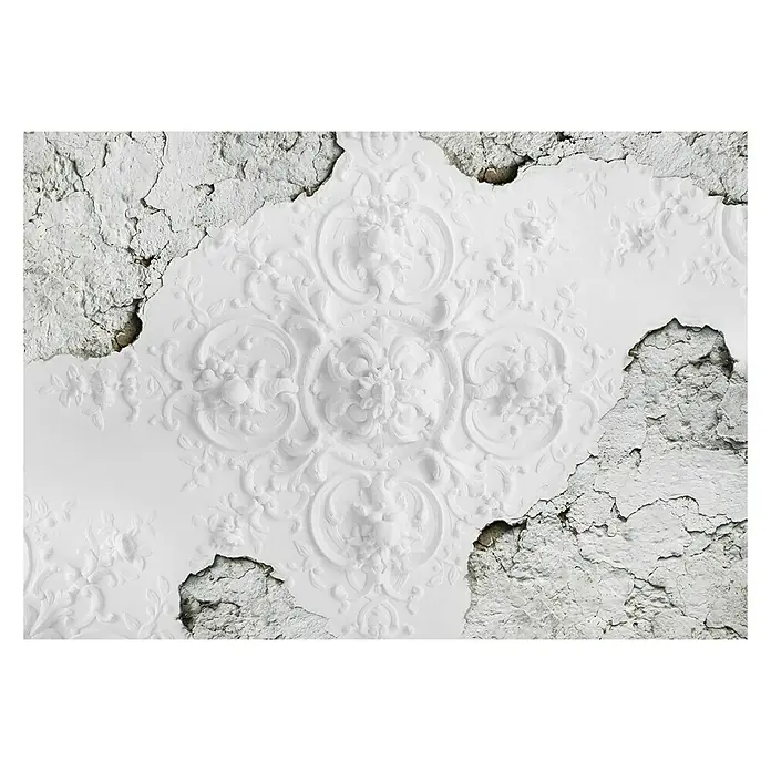 Fototapete FlachreliefB x H: 312 x 219 cm, Vlies - Detailansicht einer dekorativen, weißen Stuckdecke mit floralen Mustern und Beschädigungen, die den darunterliegenden Untergrund freilegen.