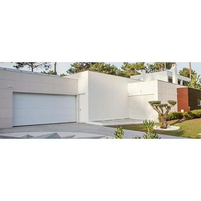 Solid Elements Garagentor Solid Pro - B x H: 2.750 x 2.125 mm, Verkehrsweiß, Glatt - Moderne Hausfassade mit großem, weißen Garagentor und gepflasterter Zufahrt, umgeben von gepflegtem Grün.