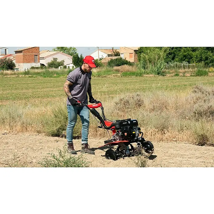 Ducati Azada de gasolina DTL7000 - 4,3 kW, 4 tiempos, Recomendación máxima de superficie: 1.500 m² - Un hombre usando una motoazada roja DUCATI en un campo para preparar la tierra, la motoazada es robusta y eficiente.