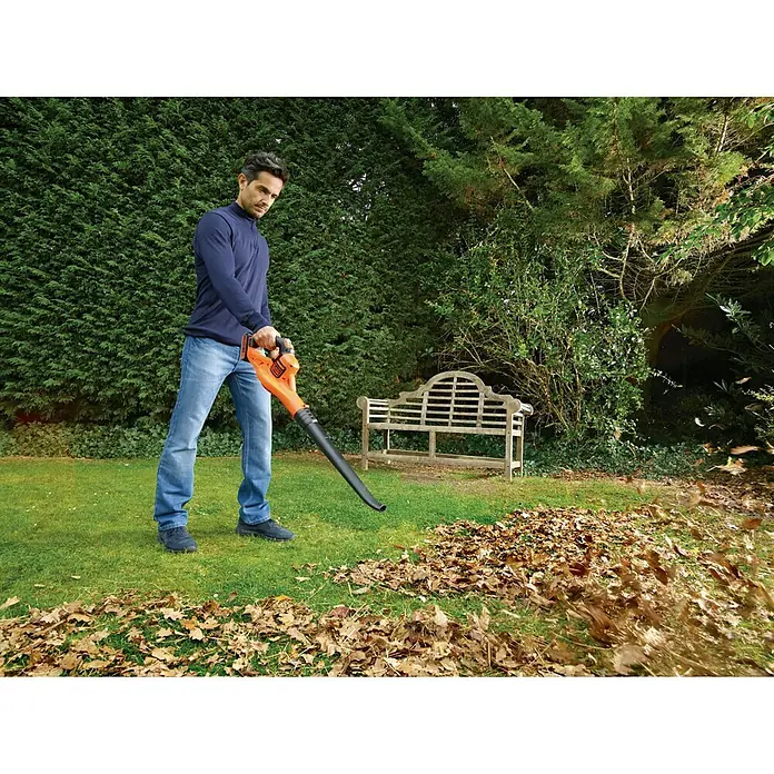 Black+Decker Soplador de hojas de batería Boost - 18 V, 2 Ah, Velocidad de soplado: 209 km/h, Potencia de soplado: 1,5 m³/min - Un hombre usa un soplador de hojas para limpiar las hojas en un jardín. La atención se centra en el uso práctico del soplador de hojas al aire libre.
