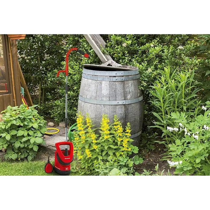 Einhell Regenfasspumpe GE-SP 3546 RB - Leistung: 350 W, Max. Fördermenge: 4.600 l/h - Der Einhell Regenfasspumpe GC-GP 6538 Set, ideal für die Gartenbewässerung, steht vor einem vollen Regenfass inmitten üppiger Vegetation.