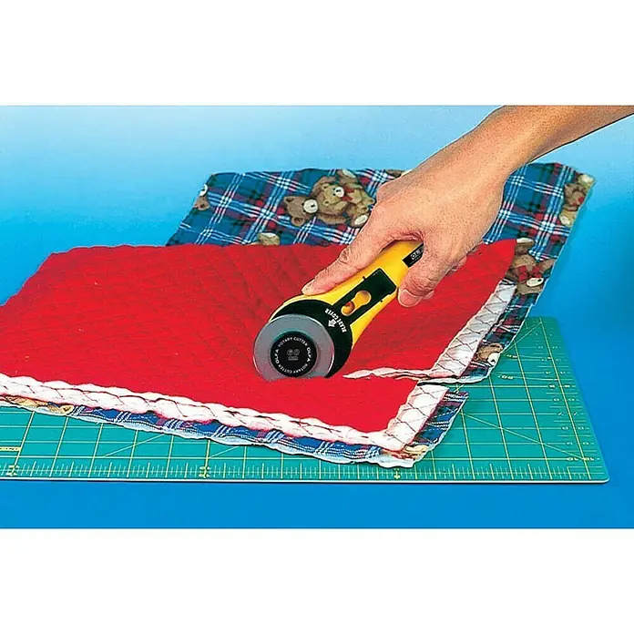 Olfa Rollschneider RTY-3/G - Klingendurchmesser: 60 mm, Werkzeugloser Klingenwechsel - Das Bild zeigt einen gelben Rollschneider, der zum Schneiden von rotem Stoff auf einer grünen Schneidematte verwendet wird.