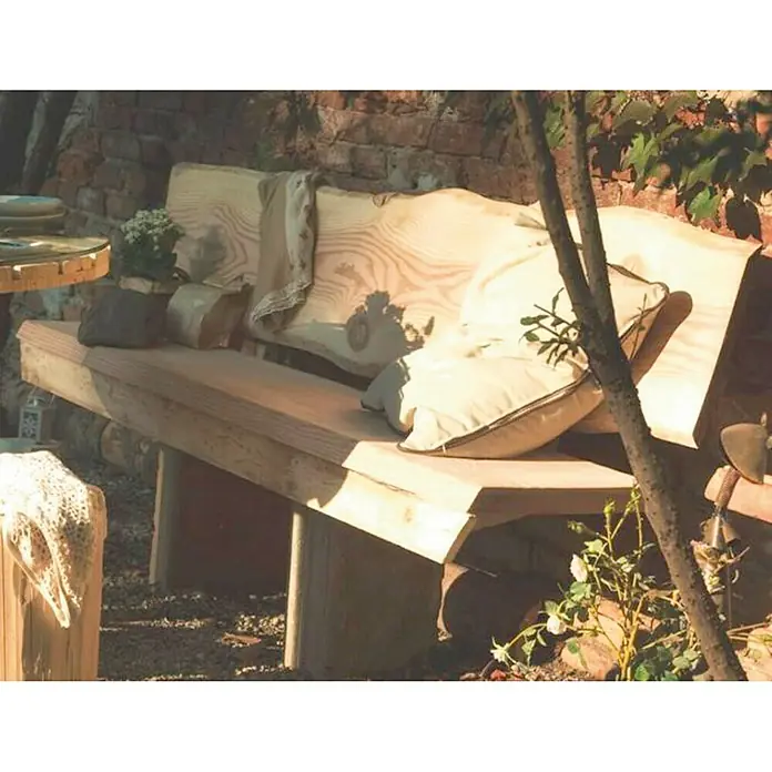Tablero de madera maciza Tarugo - Abeto rojo, L x An x Es: 120 cm x 38 cm x 50 mm, Anchura resultante: 30 cm - 38 cm - Un banco rústico de madera con cojines frente a una pared de ladrillos. El banco invita a relajarse en el jardín.