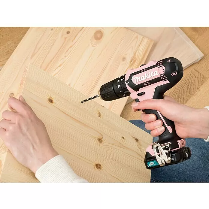 Makita Akku-Schlagbohrschrauber HP333DSAP1 - 12 V, 1 Akku, 2 Ah - Eine Person bohrt mit einem pink-schwarzen Makita Akkubohrer in ein helles Holzbrett.