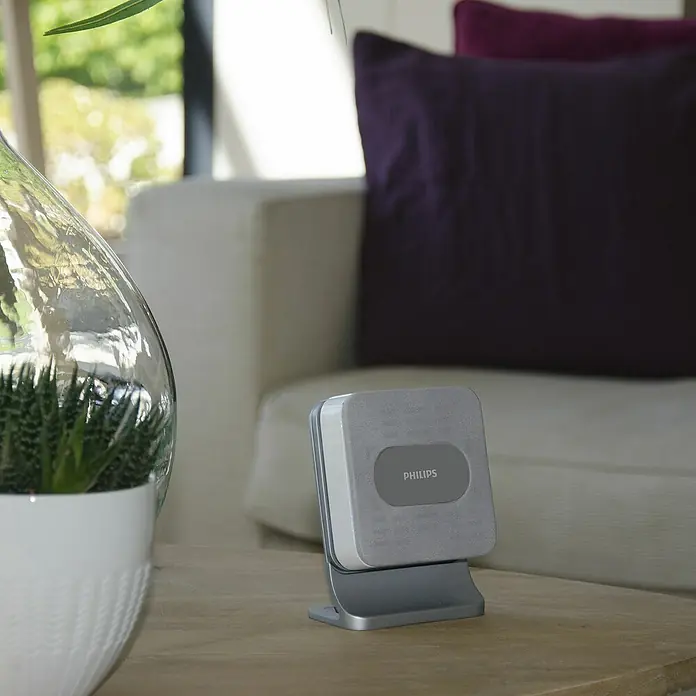 Philips Funk-Gong-Set WelcomeBell 300 Color - Reichweite Funk: 300 m, IP65, Kunststoff - Nahaufnahme eines Philips Lautsprechers auf einem Tisch, neben einer Zimmerpflanze und einem Sofa.