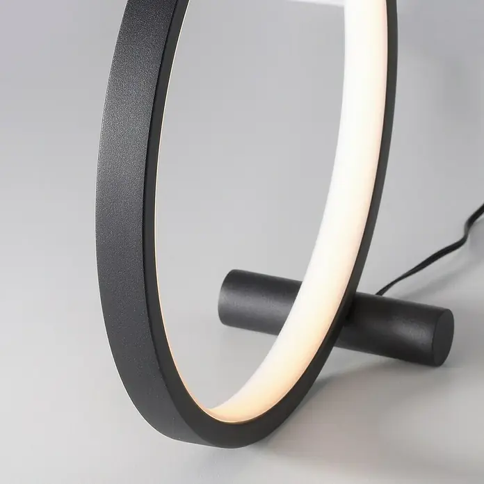 Just Light Ritus Lámpara de sobremesa redonda - 10,5 W, Ø x Al: 25,5 x 10 cm, Negro - Primer plano de una moderna lámpara de mesa LED negra en forma de anillo con base cilíndrica sobre un fondo gris.