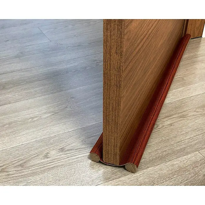 Junta para puerta Rodillo - Sapelly, Largo: 95 cm - Aislante de corrientes de aire con aspecto de madera debajo de una puerta de madera sobre un suelo de madera clara. El tope de puerta protege.