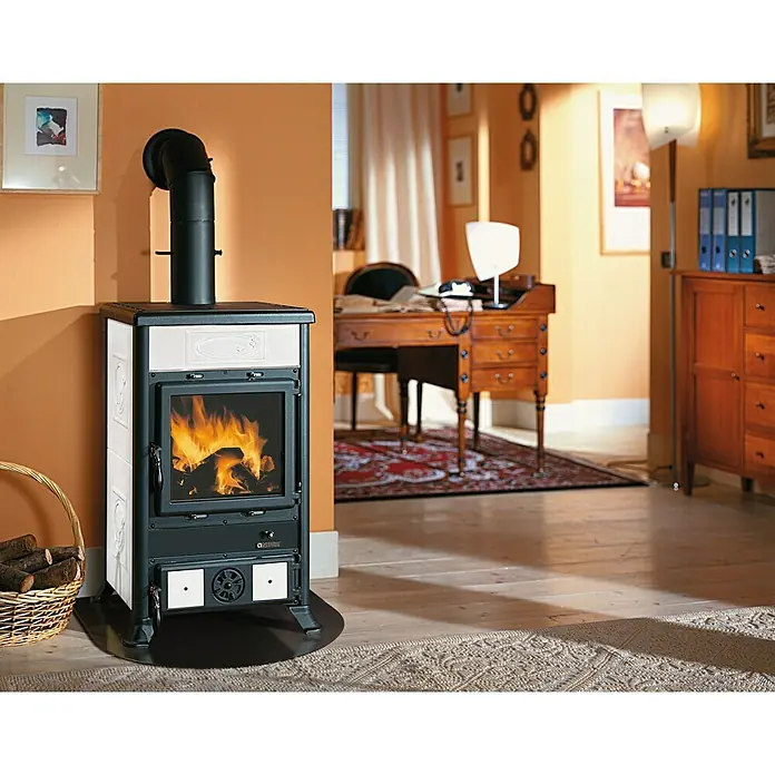La Nordica Kaminofen Rosella R1 - 11 W, Raumheizvermögen: 252 m³, Material Verkleidung: Keramik, Schwarz/Weiß - Ein Kaminofen mit weißer Verkleidung und schwarzem Rauchrohr steht in einem gemütlichen Wohnzimmer mit Holzboden und Teppich.