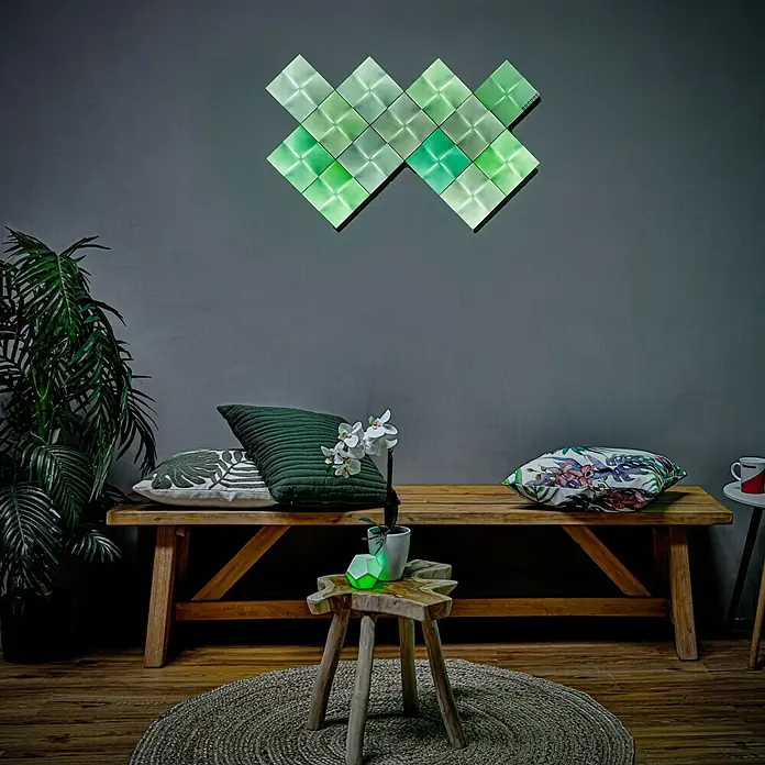Nanoleaf Erweiterungskit Canvas 4 Panels - 4 Stk., 4 W, Weiß, RGBW, Canvas, Smart Home-fähig: Ja - Ein grünes Nanoleaf Lichtpanel an einer Wand über einer Holzbank. Das Panel strahlt helles, grünes Licht aus und sorgt für Ambiente.