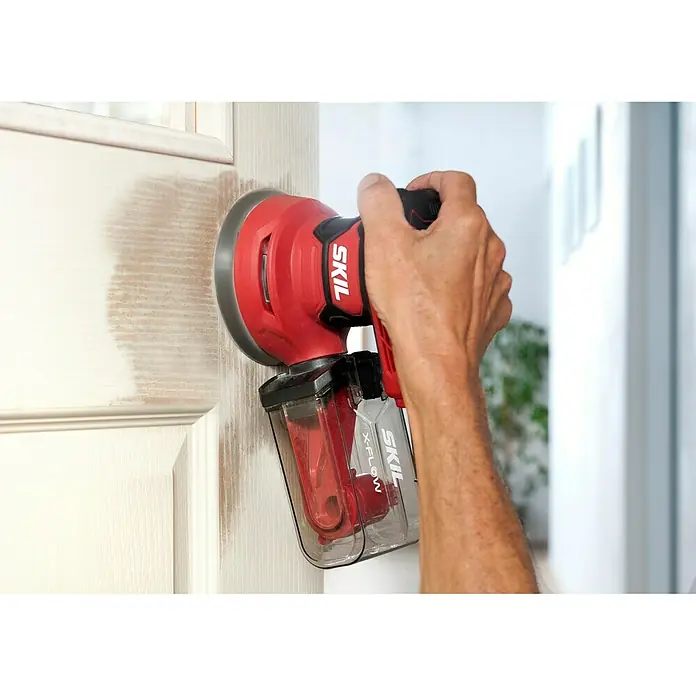 Skil Elektro-Exzenterschleifer 7471 AA - 300 W, Durchmesser Schleifteller: 125 mm - Nahaufnahme eines SKIL-Elektroschleifers, der auf einer Holztür verwendet wird, perfekt zum Schleifen verschiedener Oberflächen.