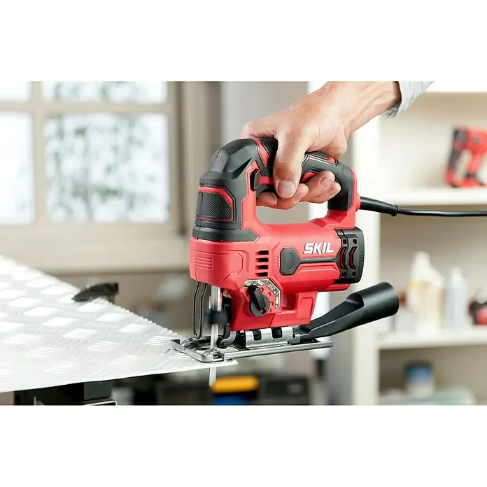 Skil Elektro-Pendelhubstichsäge 4530 AA - 0 /min - 3.000 /min, Max. Schnitttiefe in Holz: 75 mm, Anzahl Pendelhubstufen: 4 Stk. - SKIL Stichsäge in Aktion: Präzise Schnitte in ein Werkstück. Die Stichsäge ist rot und schwarz und wird von einer Hand gehalten.