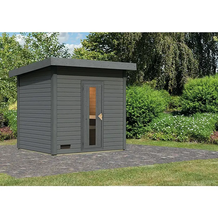 Karibu Saunahaus Hytti - Ohne Ofen, Terragrau, L x B x H: 196 x 231 x 228 cm - Das Bild zeigt eine graue Gartensauna mit Flachdach, die auf einem gepflasterten Bereich in einem Garten steht.