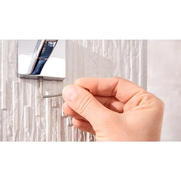 Tesa Deluxxe Handtuchhaken - Chrom, Glänzend - Ein Chrom-Wasserhahn wird mit einem Inbusschlüssel an einer strukturierten Wand befestigt, um seine Installation oder Wartung zu demonstrieren.