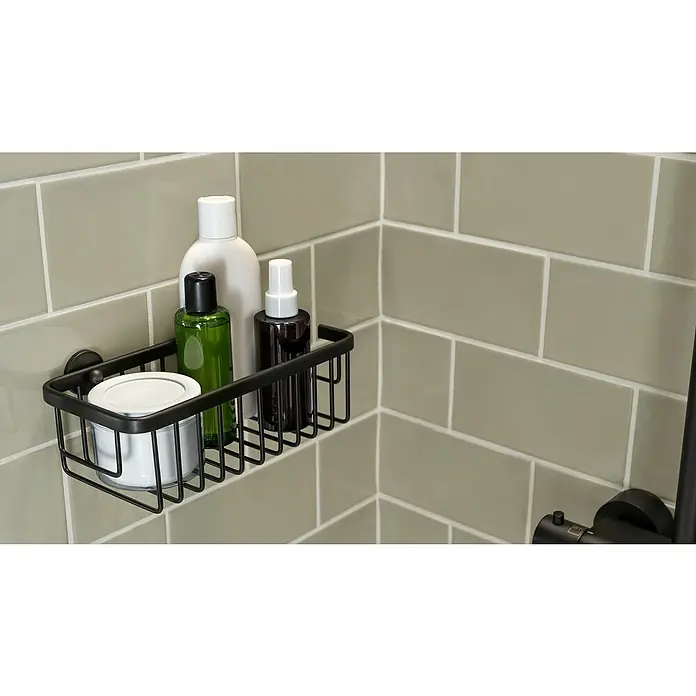 Tesa Aluxx Duschkorb - L x B x H: 12,5 x 25 x 9,2 cm, Schwarz, Matt - Nahaufnahme eines schwarzen Duschkorbs an einer gefliesten Wand, der Toilettenartikel wie Lotionen und Cremes enthält.