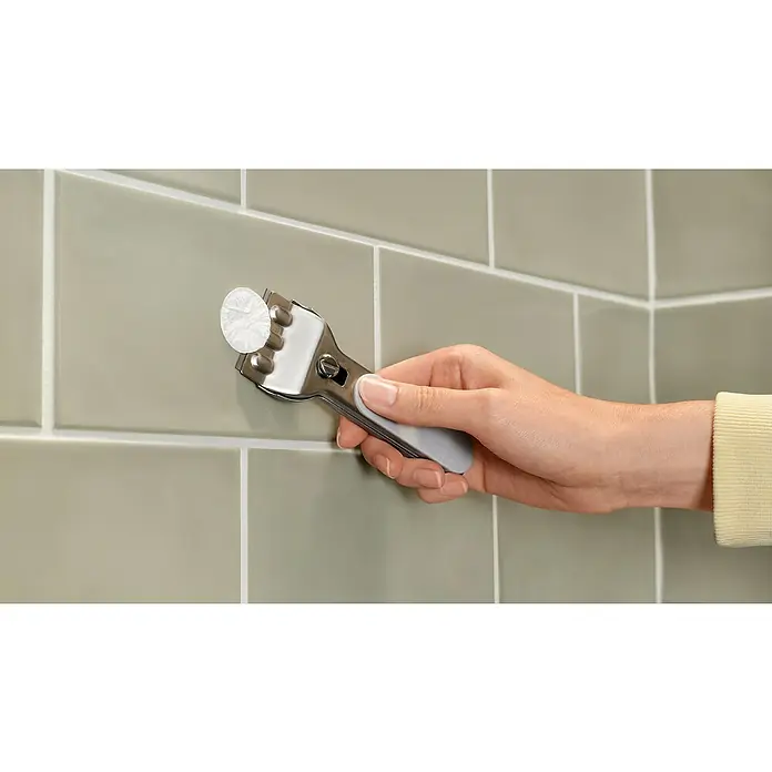 Tesa Aluxx Cesta de baño angular - L x An x Al: 16,3 x 16,3 x 26,2 cm, Negro, Recubrimiento en polvo - Una mano sujeta un rascador de vidrio contra una pared de azulejos para quitar residuos difíciles. Ideal para limpiar vidrios y azulejos.