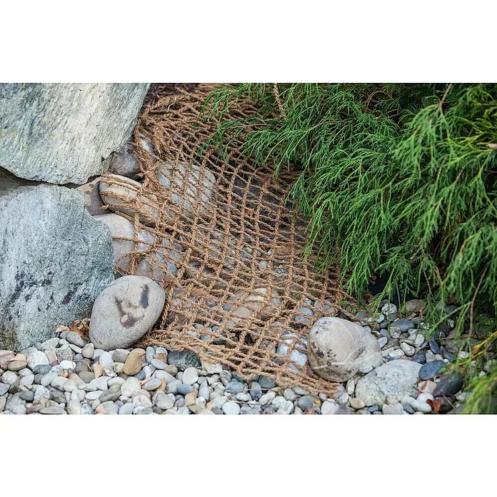 Heissner Teichnetz - Breite: 100 cm - Nahaufnahme eines Jutegewebe-Erosionsschutznetzes, das über Steinen und Kieseln in einem Garten verlegt ist, mit grünen Pflanzen im Hintergrund.