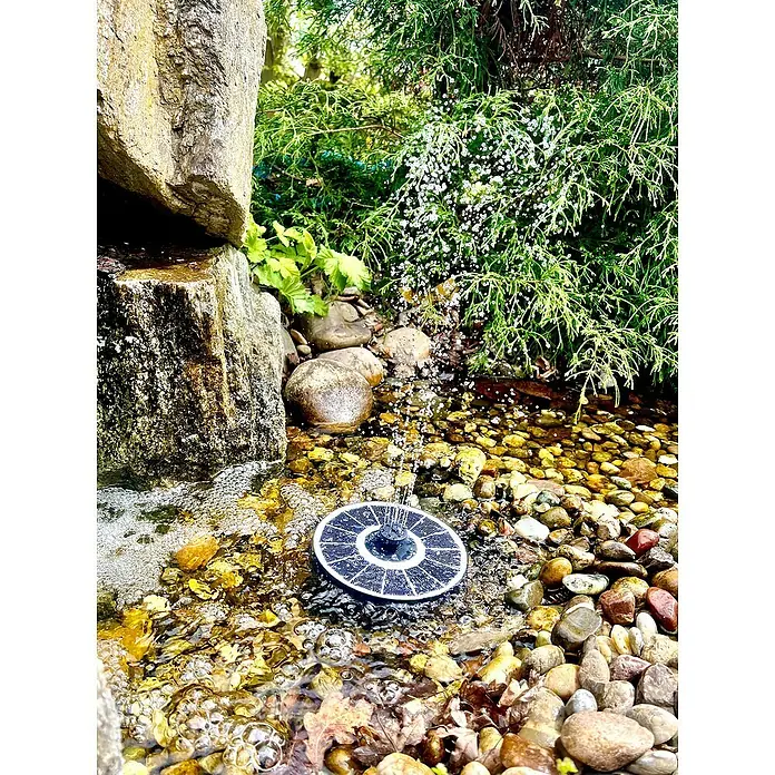 Heissner Solar-Teichpumpe - Fördermenge pro Std.: 120 l - 220 l - Bild einer Solarbetriebene Springbrunnenpumpe im Teich, umgeben von Steinen und Pflanzen. Ideal für Gartenteiche.