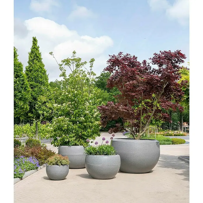 Capi Europe Übertopf rund Arc Granite - Außenmaß (Ø x H): 177 x 120 cm, Schwarz, Kunststoff, Matt - Verschiedene graue Pflanzgefäße im Freien mit Bäumen und Pflanzen. Die runden Töpfe bilden eine schöne Gartendekoration.