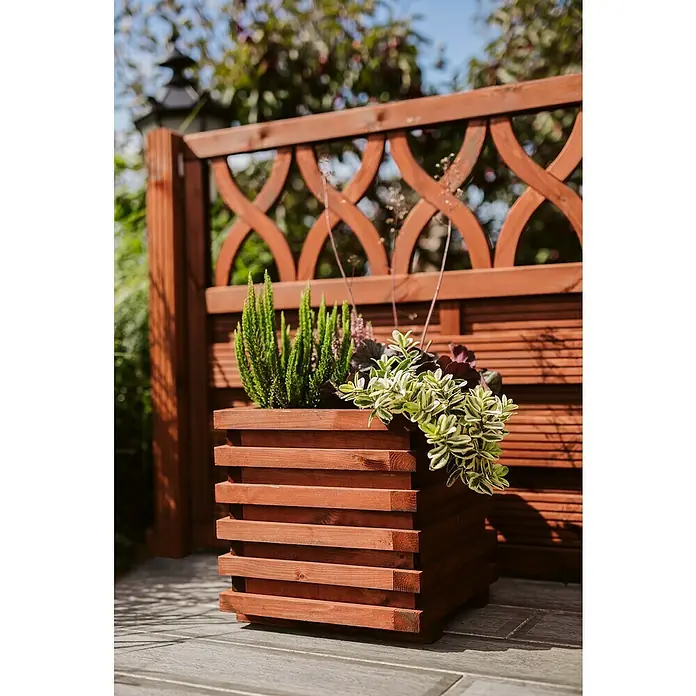 Pflanzkasten Torino - Außenmaß (L x B x H): 34 x 34 x 34 cm, Holz, Teak - Holzpflanzgefäß mit Zierpflanzen und dekorativem Holzzaun im Hintergrund, ideal für Garten oder Terrasse.
