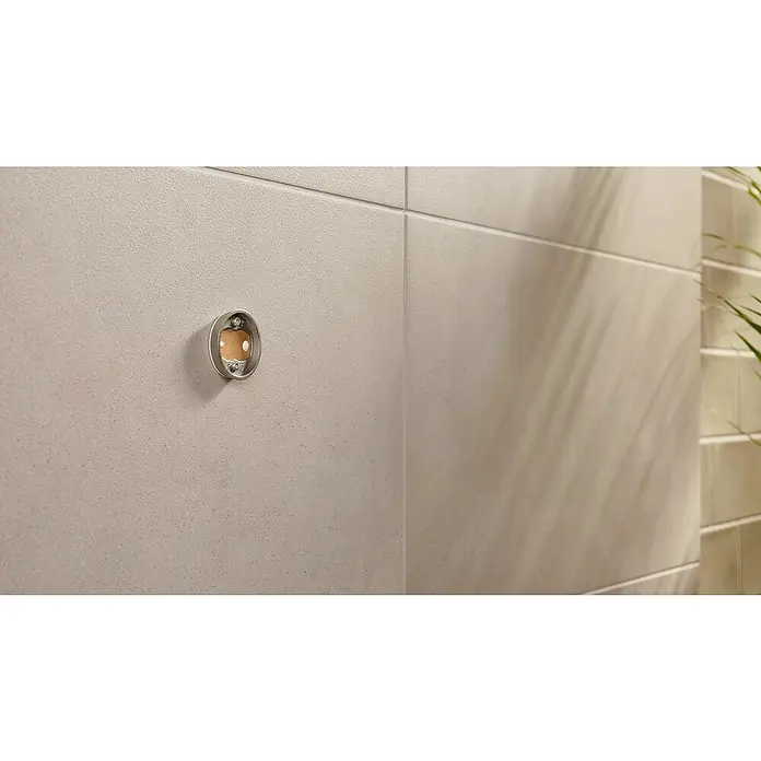 Tesa Moon Handtuchhaken - 2-armig, Graphit, Matt - Nahaufnahme einer leeren Toilettenpapierhalterung aus Edelstahl an einer Badezimmerwand, die ein minimalistisches Design zeigt.