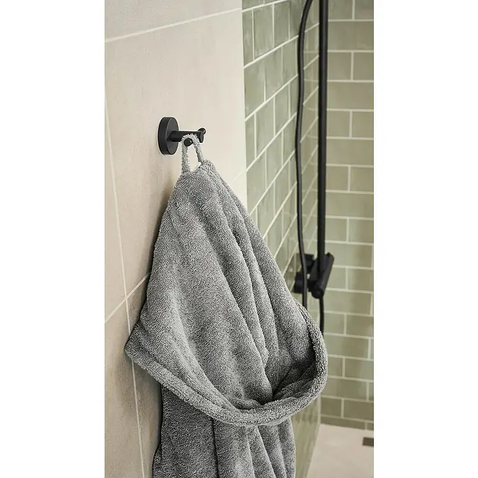 Tesa Moon Handtuchhaken - 2-armig, Schwarz, Matt - Ein grauer Bademantel hängt an einem schwarzen Haken an der Wand im Badezimmer, neben einer modernen Duscharmatur.