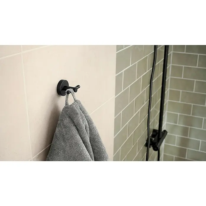 Tesa Moon Handtuchhaken - 2-armig, Graphit, Matt - Ein schwarzer Handtuchhaken mit einem grauen Handtuch, montiert an einer getäfelten Wand in einem Badezimmer mit Dusche.