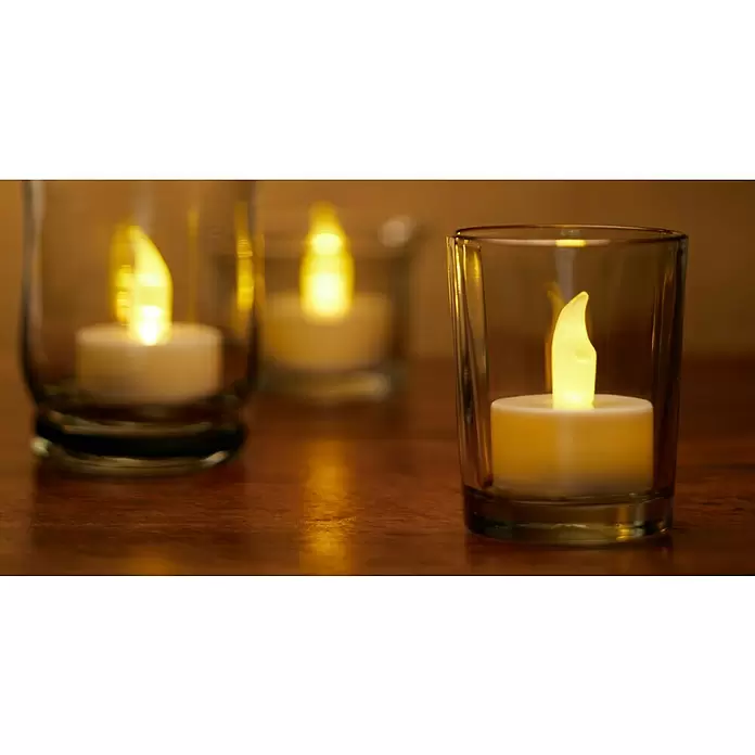 LED-Teelicht - 2 Stk., Durchmesser: 4 cm - Drei LED-Teelichter mit gelben Flammen in klaren Glasgefäßen spenden warmes Licht auf einer Holzoberfläche.