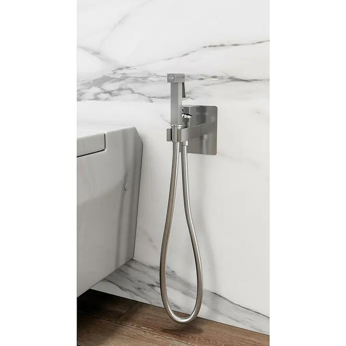 IO Orion Ducha higiénica inodoro - Cromo - Primer plano de un rociador de bidé moderno con manguera flexible y soporte de pared en un baño con paneles de mármol.
