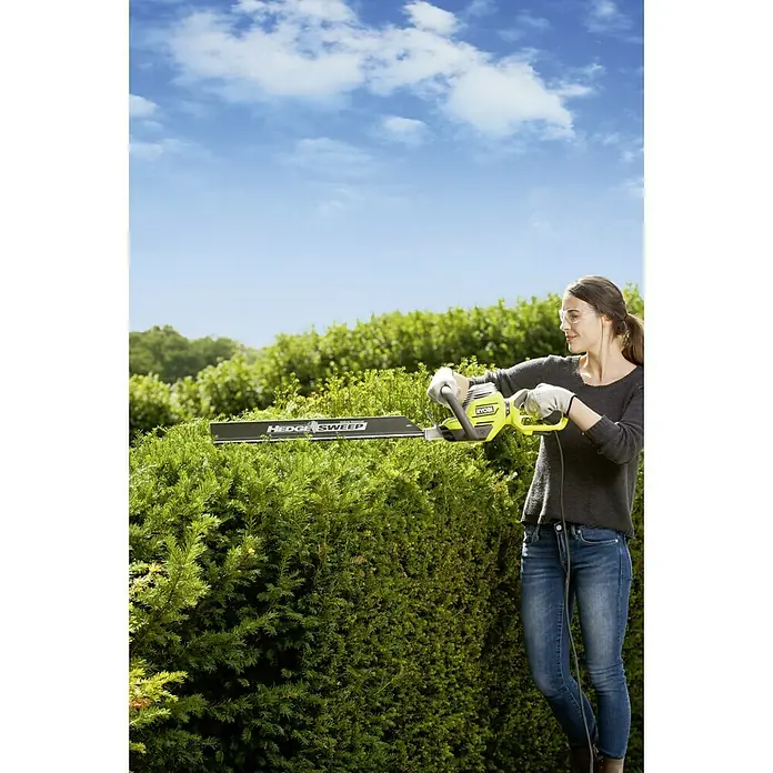 Ryobi Elektro-Heckenschere RHT8165RL - 800 W, Schnittlänge: 65 cm - Frau schneidet Hecke mit Ryobi Heckenschere, blaue Jeans, grauer Pullover. Gartenarbeit mit der RYOBI Heckenschere.