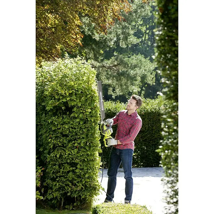 Ryobi Elektro-Heckenschere RHT8165RL - 800 W, Schnittlänge: 65 cm - Ein Mann schneidet mit einer Ryobi Heckenschere eine Hecke im Garten. Die Heckenschere ist gut sichtbar.