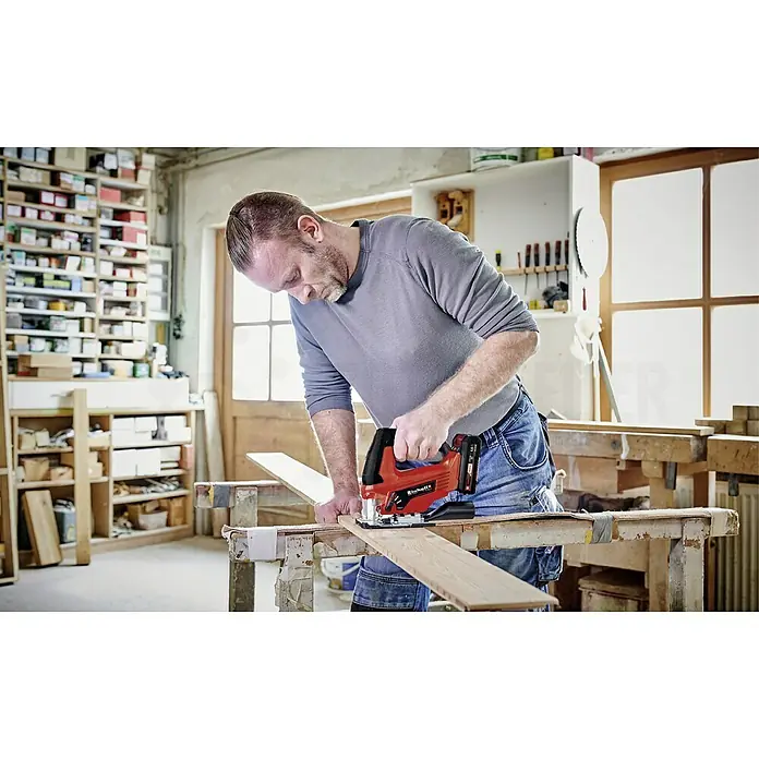 Einhell Power X-Change 18V Akku-Pendelhubstichsäge TC-JS 18 Li-Solo - 18 V, Ohne Akku, 0 /min - 2.700 /min - Ein Mann arbeitet mit einer Einhell Akku-Stichsäge an einem Holzbrett in seiner Werkstatt, wobei die rote Stichsäge gut sichtbar ist.