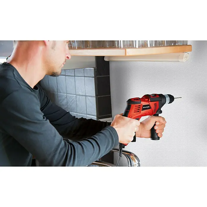 Einhell Schlagbohrmaschine TC-ID 550 E550 W, Schnellspannbohrfutter - Nahaufnahme einer roten Einhell Schlagbohrmaschine in Aktion, gehalten von einem Mann bei Reparaturarbeiten.