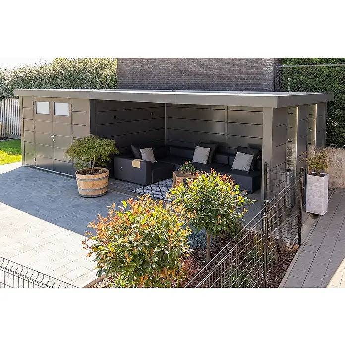 Telluria Metallgerätehaus Classico 3330 mit Lounge XL rechts inkl. 2 Fenster und Elektro-Set - Außenmaß inkl. Dachüberstand (B x T): 812 x 318 cm, Stahl, Anthrazit, Inkl. Innenwandverkleidung & Elektro-Set - Eine moderne Gartenlaube mit grauem Dach und schwarzen Wänden, ausgestattet mit einer bequemen Couchgarnitur und dekorativen Pflanzen.