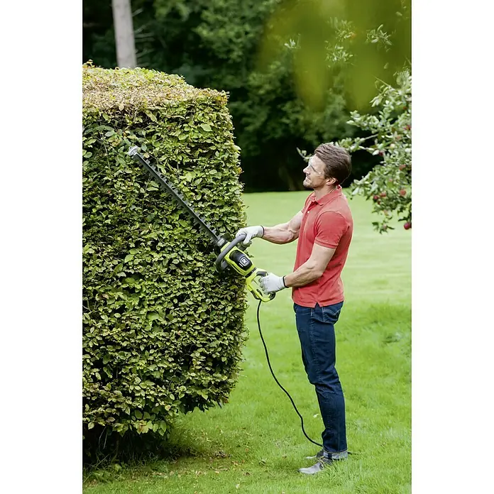Ryobi Cortasetos eléctrico RHT6160RL - 600 W, Longitud de corte: 60 cm - Hombre cortando seto con cortasetos Ryobi, asegurando resultados profesionales. Diseño ergonómico y motor potente para jardinería sin esfuerzo.