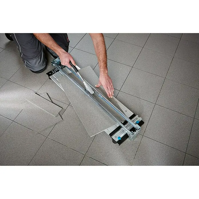 Wolfcraft Cortador manual de azulejos TC 710 PM - Longitud de corte máx.: 710 mm, Espesor máx. de azulejo: 14 mm - Un hombre corta azulejos con un cortador de azulejos sobre un suelo de baldosas. La herramienta hace un corte preciso en el azulejo.