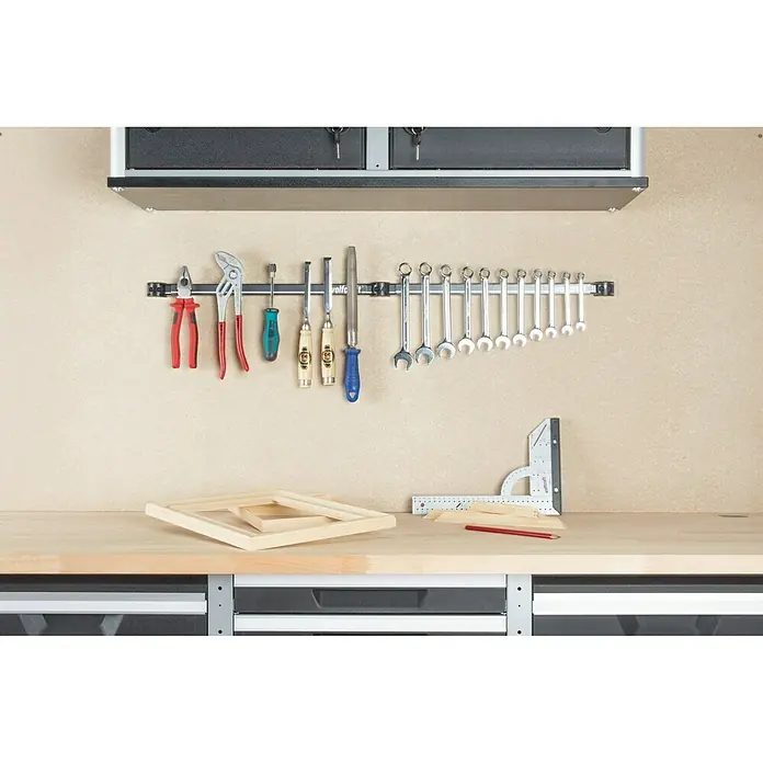 Wolfcraft Barra magnética 6806000 - Largo: 46 cm - Herramientas colgadas en una barra magnética sobre un banco de trabajo con cajones, debajo hay marco de madera, lápiz y escuadra.