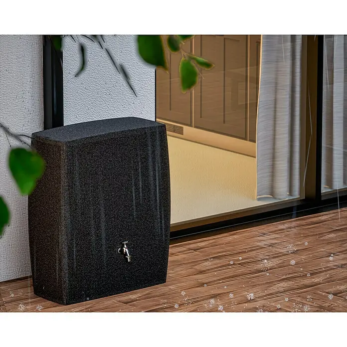 Arves Regenspeicher Boxy - 720 l, Granitkörnung, 1 Stk. - Eine Regentonne in Granitoptik mit Messingarmatur steht auf einem Holzdeck vor einer Terrassentür. Nutzen Sie Regenwasser zur Gartenbewässerung.