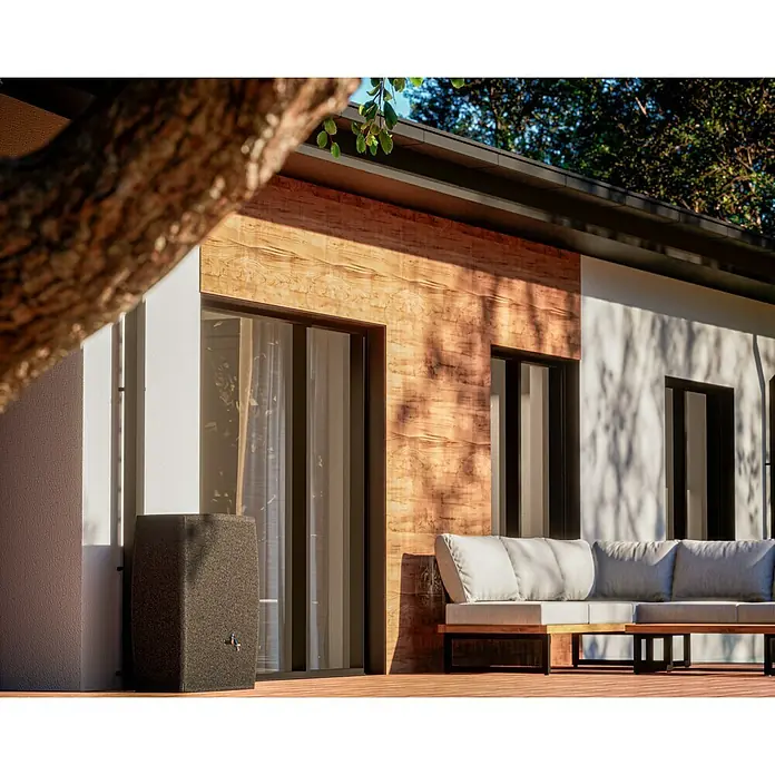 Arves Regenspeicher Boxy - 720 l, Granitkörnung, 1 Stk. - Stilvolle Regenwassertonne vor einem modernen Haus mit Holzverkleidung und einer grauen Gartenlounge für entspannte Stunden im Freien.