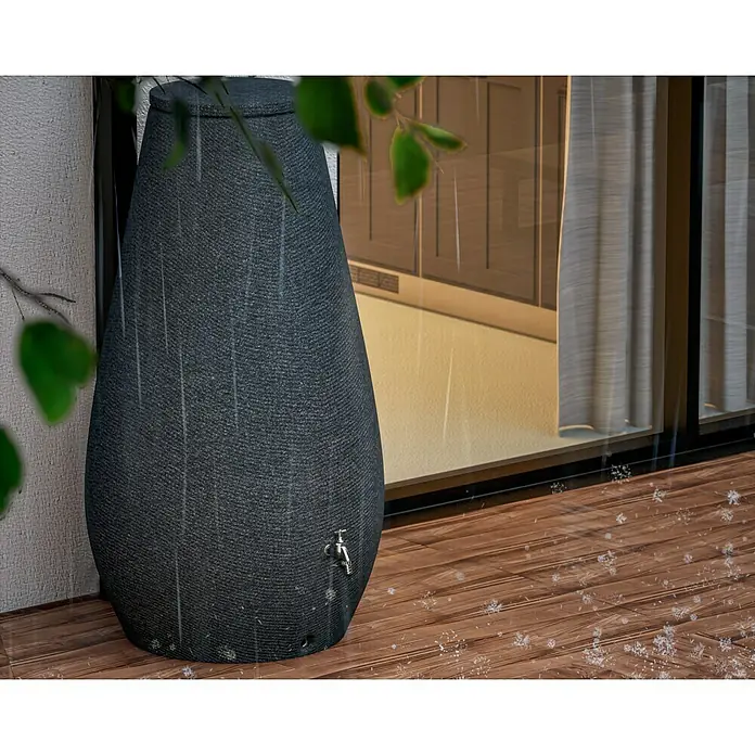 Arves Regenspeicher Drop - 410 l, Granitkörnung, 1 Stk. - Eine stilvolle graue Regentonne mit einem Hahn, die auf einer Holzterrasse im Regen steht. Praktische Wasserspeicherung für den Garten.